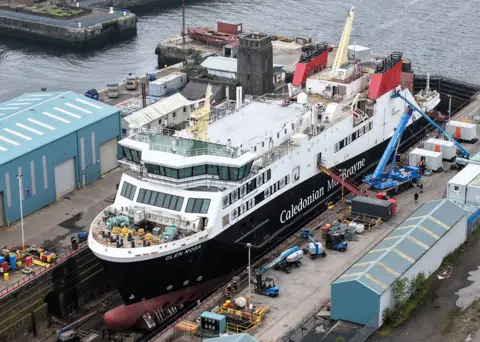 Christopher Brindle A large black white and red ship in a dry dock with cranes beside it
