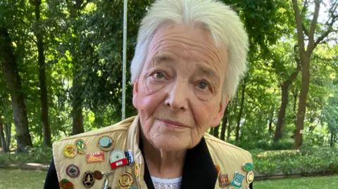 Tom Ingall/BBC Aggie Currie wearing a gilet covered in historic activist's badges.