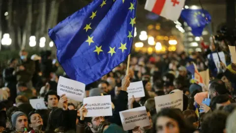 AFP Protesters brandish placards and a European Union flag as they demonstrate in front of the Georgian parliament, in Tbilisi on March 7, 2023