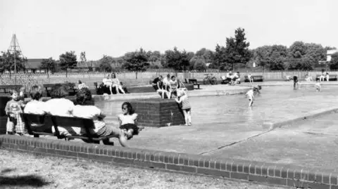 Nottingham City Council A 1995 shot of adults relaxing by the pool with a handful of children walking in it