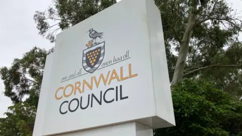 The Cornwall Council logo on a white sign. The logo is a mix of orange and black in colour.