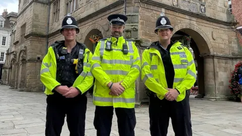 West Mercia Police Three police officers in high visibility vests stood in a market square and smiled for the camera