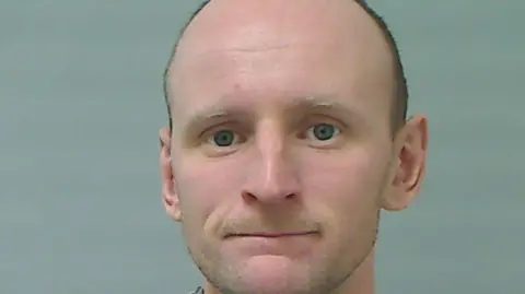 Noel Logan, a man who is balding with dark hair and blue/grey eyes.