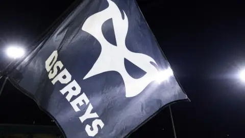 Ospreys flag under floodlights during a night game