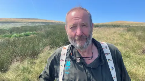 Photograph of the National Trust ranger Nick Taylor. He is pictured in front of wetland reeds on Holcombe Moor.