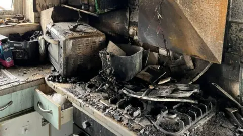 Oxfordshire Fire and Rescue Melted pan and blackened kitchen items on kitchen hob charred microwave and soot covering egg-shell blue kitchen drawers