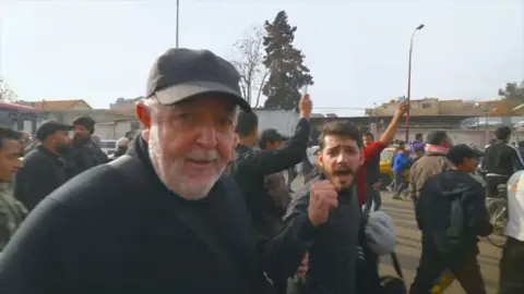 Jeremy Bowen walking with a crowd of people in Damascus heading towards what they believe is a public execution