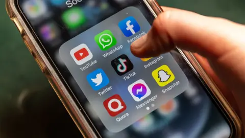 A phone screen showing several social media platforms with someone's finger hovering over TikTok icon