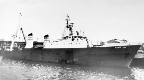 PA Media A black and white image of the vessel which has a dark hull and white platforms atop. There is a tall triangular equipment erected at the back of the ship. The main quarters are closer to the front. There is antennae at the top and sectioned lined with windows below it.