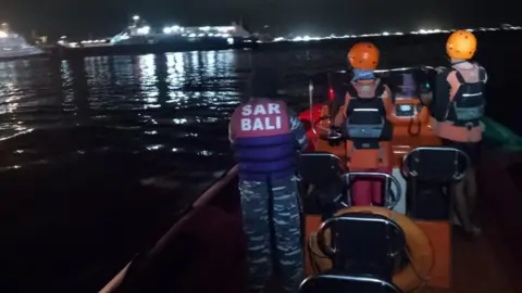 Bali Search and Rescue Rescuers wearing orange helmets on a boat. They are sailing in waters in the dark.