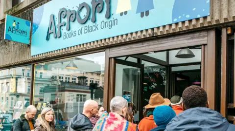 D Pamben A crowd of people gather outside Afrori bookshop, which has a blue and black sign