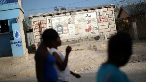 Reuters Women walk past an Oxfam sign in Corail, a camp for displaced people of the 2010 earthquake, on the outskirts of Port-au-Prince, Haiti, February 13, 2018.