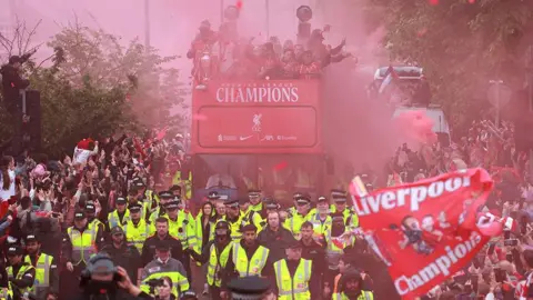 Reuters Liverpool FC players on an open top bus in Liverpool city centre celebrating after winning the Premier League with a number of police officers around the vehicle and fans cheering lining the route. 