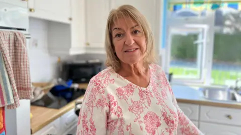 Kay Lindsay pictured with short blonde hair. She is wearing a white v-neck top with red flowers on.