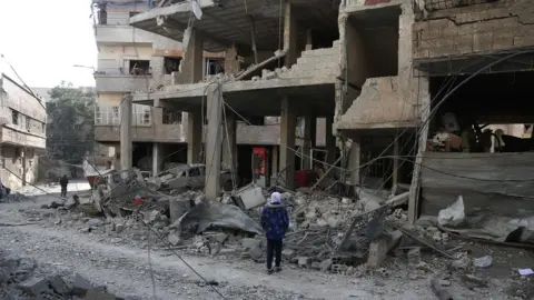 AFP A Syrian girl looks at the rubble of a hospital that was destroyed in a reported government air strike in Hamouria, in the besieged rebel-held Eastern Ghouta (21 February 2018)