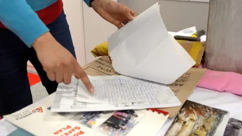 A hand points at a handwritten letter in a pile of documents