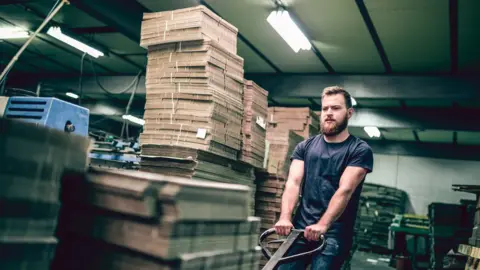 Getty Images Tired Worker Pushing Cardboard Carton Planks On Transportation Cart on Night Shift