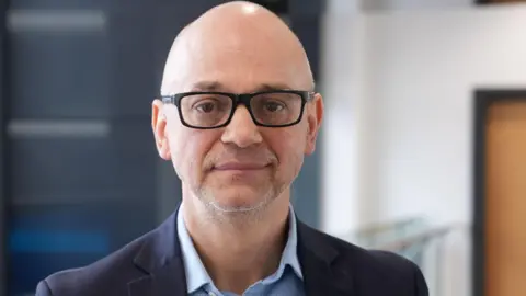 A man with glasses wearing a navy jacket looking at the camera