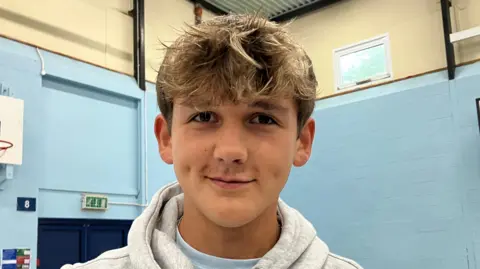 Launceston College pupil Aaron smiling at the camera. He is wearing a light grey hoodie and a light blue T-shirt