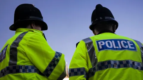 A back and side profile of two British Police officers wearing yellow high visibility jackets