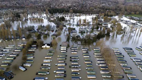 PA Media An aerial photo of the flooded Billing Aquadrome Holiday Park. There are more than 100 static caravans with flood water up to their windows and the whole site is deep in brown flood water. Houses in Northampton can be seen in the distance. 