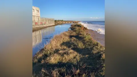 TASC A picture showing waves over-topping the grassy dunes in front of the Sizewell C site. 