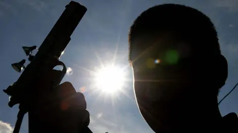A silhouette of a young man holding a gun