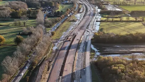 Shaun Whitmore/BBC A drone photograph of the A47 work at Blofield. To the left is the existing single-carriageway road. Next to it are the new carriageways, still under construction. There is a lot of standing water following heavy rain.
