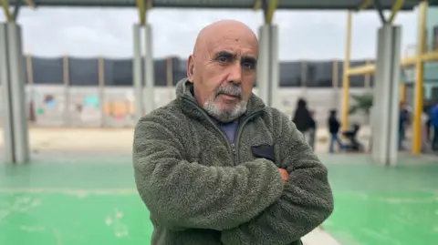Chilean voter Ricardo Herrera, wearing a green fleece jacket, stands with his arms folded, looking at the camera.
