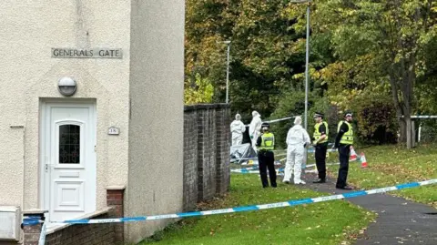 Uniformed police officers and foernsic officers in white overalls standing outside a taped-off house on General's Gate