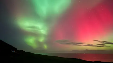 Green and pink skies are reflected in the sea and the headland is in silhouette. 