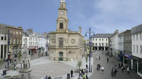 Pacemaker Coleraine town centre. There are shops on either side of the squre and people walking on the street. The sky is blue. 