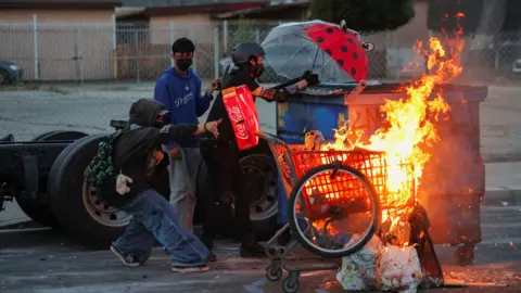 Protesters stand next to a burning shopping cart during a standoff between police and protesters