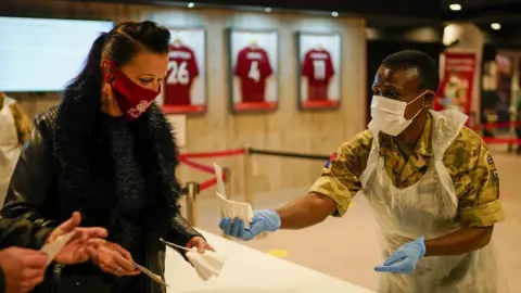 Getty Images A member of the Royal Artillery hands a test to people at a testing centre at Liverpool Football Club's Anfield stadium