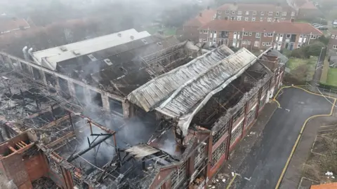 Shaun Whitmore/BBC An aerial picture taken from above the derelict shoe factory on Dibden Road in Norwich. Smoke can still be seen coming off the building. Parts of the roof have collapsed and others are burnt and charred. 