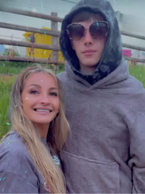 Family photo Tristan Shae Kerr, wearing glasses and a grey hooded top. He has his arm around a woman with blonde hair.