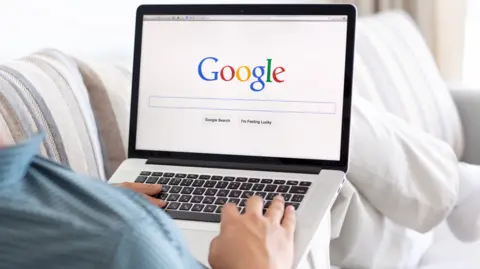 Person sitting on a couch searching Google on a laptop 