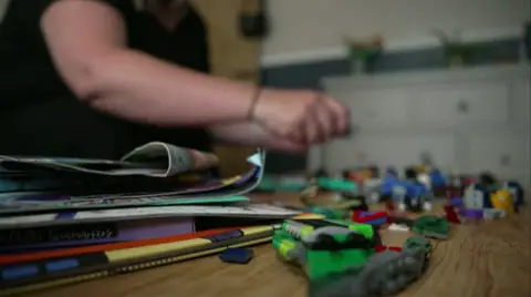 A woman is handling pieces of Lego which are spread over a coffee table but you can only make out her hands, arms and part of her torso as her identity is hidden