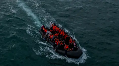 An image taken from a drone shows an inflatable dinghy packed full of migrants  wearing orange life vests making its way towards the UK in the English Channel