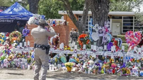 EPA A Texas Highway Patrol officer takes cell phone pictures of the memorial to the victims following the mass shooting at the Robb Elementary School in Uvalde, Texas