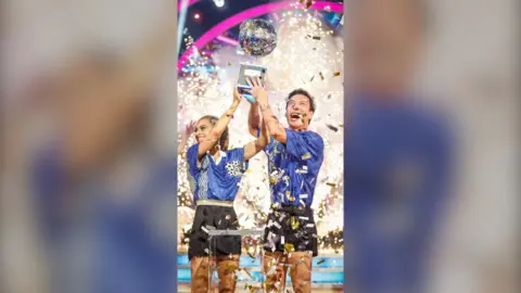 Karen Carney and her dance partner hold the Strictly trophy on set, with confetti.