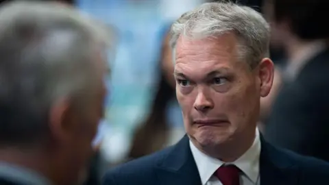 Getty Images Labour candidate Richard Tunnicliffe looks on during the count at Caerphilly Leisure Centre - he is wearing a navy blue suit with a white shirt and a red tie and is pulling a face that indicates uncertainty or displeasure.