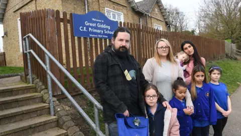 Warren Gunn/Cambs Live Parents stand with their children outside Great Gidding School Cambridgeshire