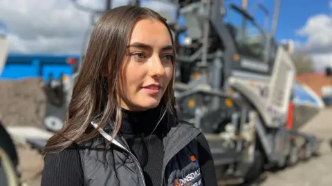 BBC/John Bowness Georgia Coleman standing in front of one of the company's resurfacing machines