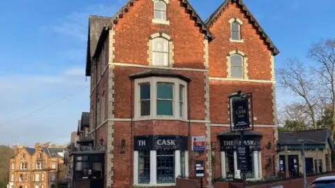 The Cask Inn. A three story red brick building with black signage displaying in white lettering The Cask.