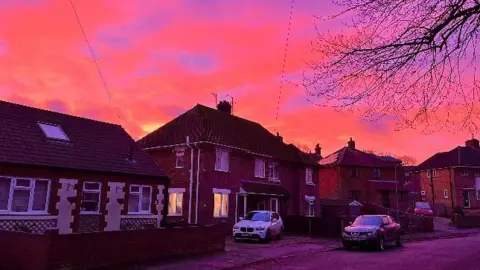 Walking Tractor A row of homes in Cromer with cars outside. The sky is a vivid orange with sections of purple