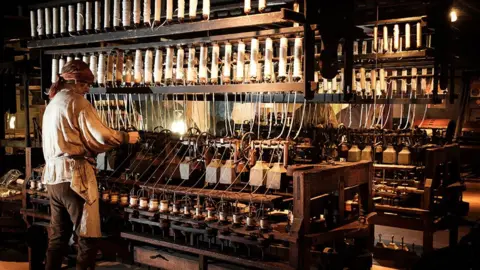 LCC A man in period dress working on a huge machine spinning reels of cotton inside Helmshore Mills Textile Museum