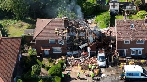 Three houses at a suspected gas explosion site in Middlesbrough. The house that exploded is in the middle and almost destroyed. Debris is at the front and there emergency workers at the scene. Roof tiles are missing from neighbouring homes
