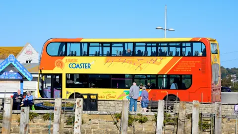 Getty Images Tourists aboard a Jurassic Coaster bus in the harbour area, West Bay, Dorset on a sunny day