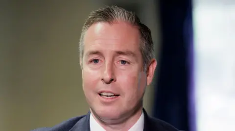 PA Media Paul Givan - grey and white haired man in a navy suit with a white shirt. 